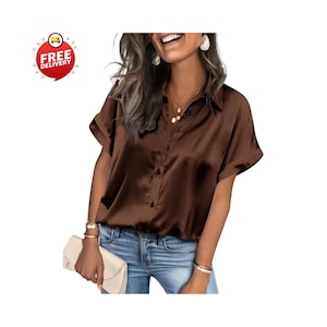 May include: A brown satin button-down shirt with short sleeves. The shirt has a classic collar and a smooth, shiny texture. The model is wearing the shirt with blue jeans and a cream-colored clutch.