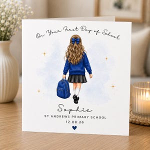 May include: A square greeting card featuring an illustration of a child with long wavy hair and a blue bow, wearing a blue jumper, grey skirt, and white socks, carrying a blue backpack. Text reads: On Your First Day of School, Sophie, ST ANDREWS PRIMARY SCHOOL, 12.08.26.