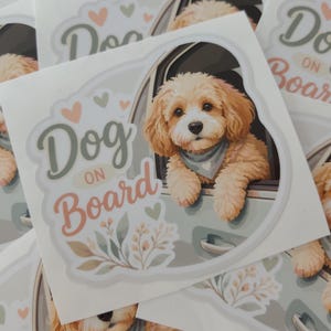 Op de afbeelding: Een rechthoekige sticker met een lichtbruine hond met krullend haar die een blauwe bandana draagt en uit een autoraam leunt. De tekst "Dog on Board" is gedrukt in een gestileerd lettertype, omringd door kleine hartjes en bloemen.