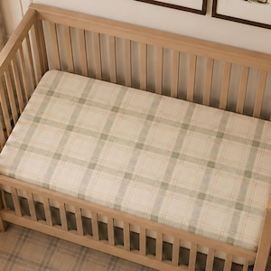 May include: A wooden cot featuring a mattress covered in a cream and sage green plaid sheet. The cot has vertical slats and a natural wood finish. Above the cot, three framed illustrations depict teddy bears playing golf in various poses.