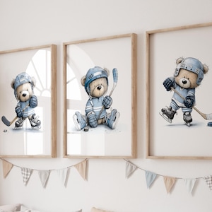 May include: Three framed watercolor prints of teddy bears playing hockey, each in a different pose. The bears wear blue hockey gear and helmets. Below the prints is a wooden storage unit with white bins and pillows.