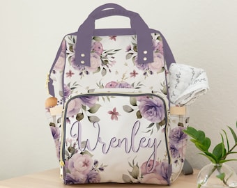 May include: Purple floral print diaper bag with a zippered pocket and the name "Wrenley" written in purple script.
