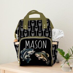 May include: A black and green diaper bag with a white arrow pattern. The bag has a large pocket on the front with the name "MASON" and two fish illustrations.