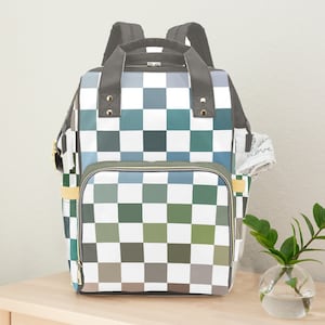May include: A backpack featuring a chequered pattern in green, blue, grey, and white squares. It has a top handle, adjustable straps, and a front zip pocket. A side pocket holds a white cloth with the word "love" printed on it.