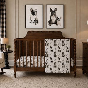 May include: A nursery with a dark wood crib, a rocking chair, and framed black and white dog art. The crib has a patterned blanket and fitted sheet with dog illustrations. A dresser and a side table with a lamp complete the room.