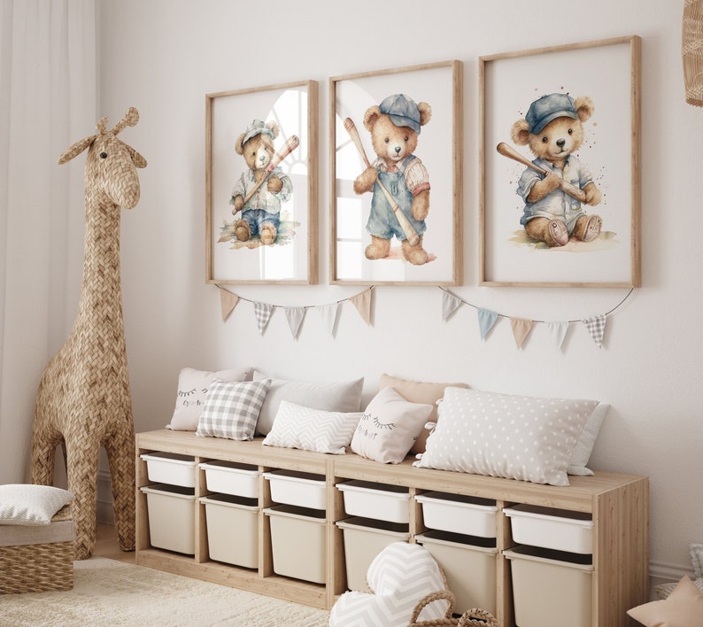 Op de afbeelding: Drie aquarelprints van teddyberen die honkbal spelen. Elke print toont een bruine teddybeer met een blauwe honkbalpet en een trui, die een houten knuppel vasthoudt. De prints zijn ingelijst in licht hout en hangen aan een witte muur.