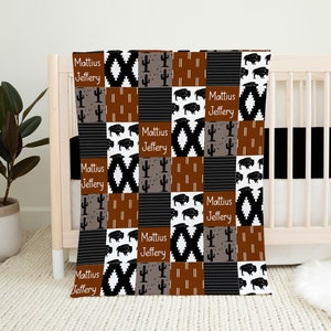 May include: A brown, black, and white baby blanket with a patchwork design featuring buffalo, cacti, and geometric patterns. The blanket has the names "Mattius Jeffery" repeated throughout.