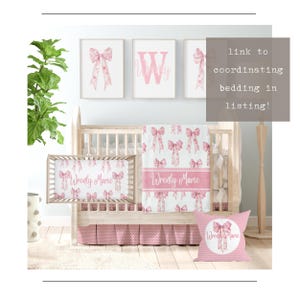Pode incluir: Um conjunto de roupa de cama para ber&ccedil;o rosa e branco com estampa de la&ccedil;o de aquarela. O conjunto inclui um len&ccedil;ol para ber&ccedil;o, um cobertor e um travesseiro. O len&ccedil;ol para ber&ccedil;o e o cobertor t&ecirc;m o nome "Wrently Marie" bordado. O travesseiro tem um c&iacute;rculo rosa com um la&ccedil;o e o nome "Wrently Marie" bordado. O conjunto &eacute; exibido em um ber&ccedil;&aacute;rio com uma parede branca e uma planta verde.