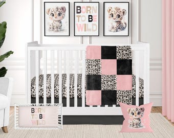 May include: A pink, black and brown leopard print cot bedding set with a pink and black chequered blanket. The set includes a cot sheet, a cot skirt, a pillow and a blanket. The cot bedding set features a cute leopard print design with the words "Born to Be Wild" on the pillow and blanket.