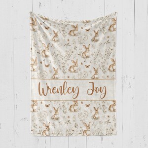 May include: A white fleece blanket with a brown bunny rabbit pattern and the names "Wrenley Joy" printed in brown text.