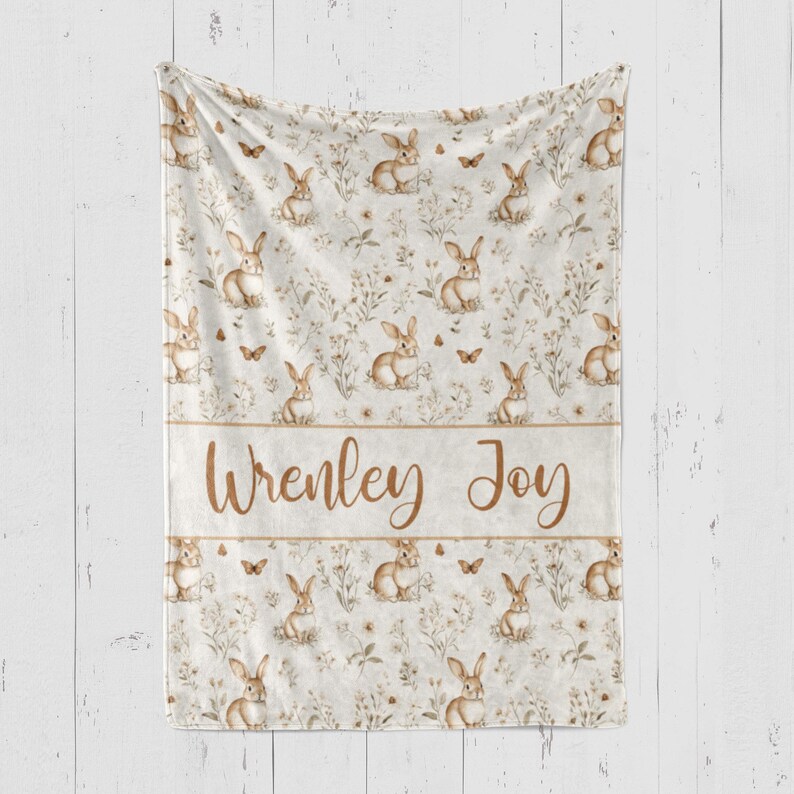 May include: A white fleece blanket with a brown bunny rabbit pattern and the names "Wrenley Joy" printed in brown text.