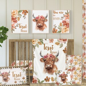 以下が含まれることがあります： オレンジ、ピンク、イエローの色合いの水彩画の花々に囲まれた、花冠をかぶったハイランド牛が特徴の、ナーサリーデコレーションセット。セットには、ブランケット、枕、そして「テッシ・レネー」と「あなたはとても愛されている」というテキストが書かれた額装されたプリント3枚が含まれています。