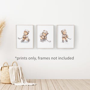 May include: Set of three prints featuring watercolour illustrations of teddy bears playing hockey. Each print shows a different pose of the bear with a hockey stick and puck. The prints are in white frames with a white background.