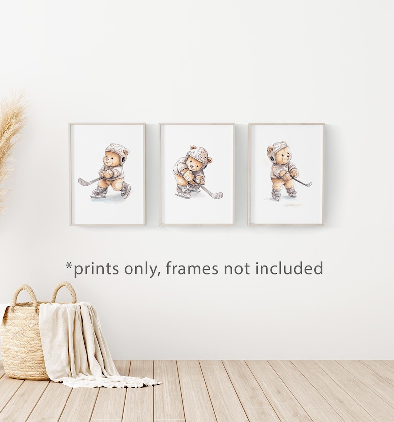 May include: Set of three prints featuring watercolour illustrations of teddy bears playing hockey. Each print shows a different pose of the bear with a hockey stick and puck. The prints are in white frames with a white background.