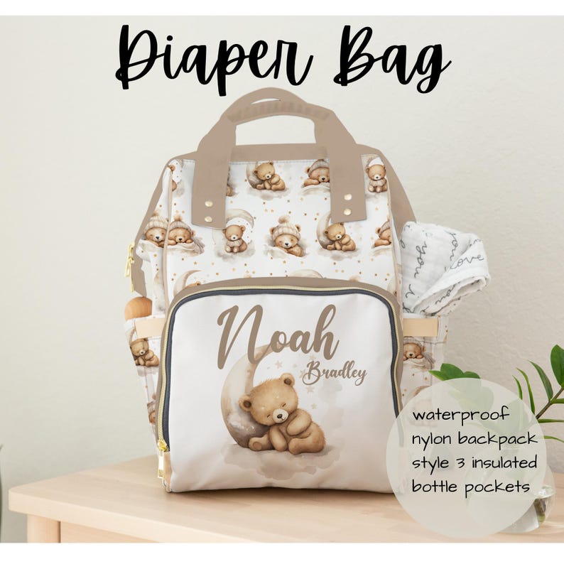 May include: A beige and white diaper bag featuring a teddy bear and moon design. The bag has a top handle and multiple pockets, with the name "Noah Bradley" printed on the front. The text "Diaper Bag" is at the top.