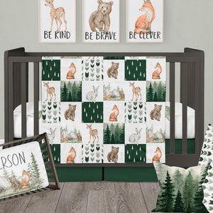 May include: A green and white cot bedding set with a woodland animal theme. The bedding features a patchwork design with images of foxes, deer, bears, and rabbits. The set includes a quilt, a pillow, and a cot skirt.