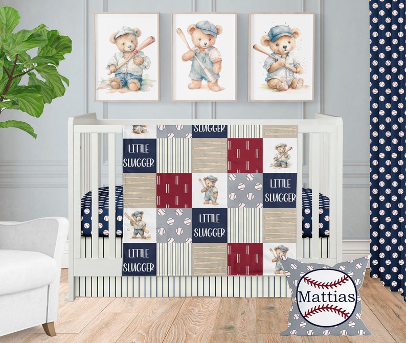 Op de afbeelding: Een babybedje met een blauw-wit gestreepte bedrok en een patchworkdeken met honkballen, beren en de woorden "Little Slugger". Een kussen met een honkbal en de naam "Mattias" ligt op de vloer.