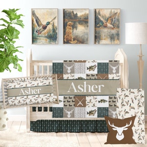 May include: A baby crib bedding set with a woodland theme. The set includes a quilt, a fitted sheet, a crib skirt, a pillow, and a pillowcase. The quilt features a patchwork design with images of deer, fish, and ducks. The fitted sheet and pillowcase have a pattern of ducks. The crib skirt has a pattern of arrows. The pillow has a brown deer head design. The set is personalized with the name "Asher".