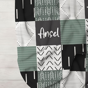 May include: A black and green baby blanket with a patchwork design. The blanket features geometric patterns and the name "Ansel" in white lettering.