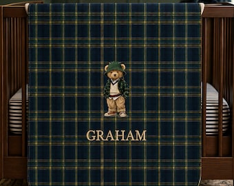 May include: A dark navy blue and green plaid blanket featuring a central graphic of a teddy bear wearing a green bucket hat, a plaid jacket, and tan trousers. The name GRAHAM is embroidered in gold capital letters below the teddy bear graphic.