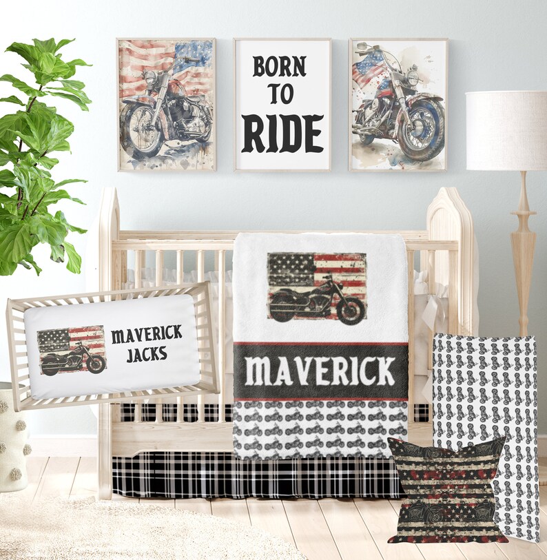 May include: A baby crib bedding set with a black and white plaid crib skirt, a white blanket with a red, white, and blue American flag and a motorcycle design, a white pillow with a red, white, and blue American flag and a motorcycle design, and the text "Maverick Jacks", and a white pillow with a black and white motorcycle pattern.