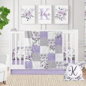 May include: A patchwork baby quilt featuring alternating squares of light purple, solid gray, and white fabric with floral patterns of purple flowers and dark berries. A matching square throw pillow displays a large letter K in a circular center.