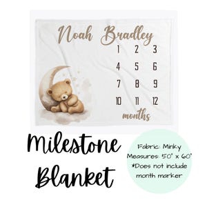 May include: White milestone blanket with the name "Noah Bradley" in brown script. Features a teddy bear on a crescent moon, numbers 1-12, and the word "months". Measures 127cm x 152cm.