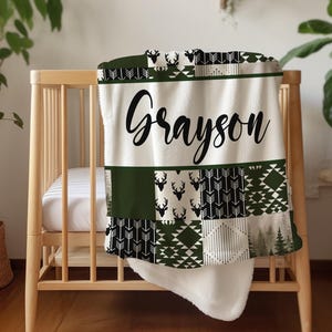 May include: A white and green patchwork baby blanket with a black and white deer pattern and the name "Grayson" in black lettering.