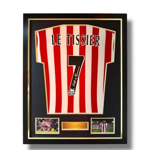 May include: Framed football shirt with red and white stripes, the number 7, and the name "LE TISSIER" in black. Includes two small photos and a plaque with the name "MATT LE TISSIER". The frame is black with a gold inner border.