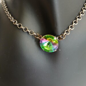 May include: A silver-toned chain necklace with a large, iridescent, oval-shaped pendant. The pendant displays a spectrum of colors, including green, yellow, and purple. The necklace is displayed on a black mannequin.