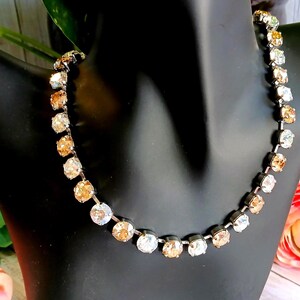 May include: A sparkling necklace with a silver-tone chain and alternating clear and champagne-colored crystals. The necklace is displayed on a black mannequin bust, with pink roses and greenery in the background.