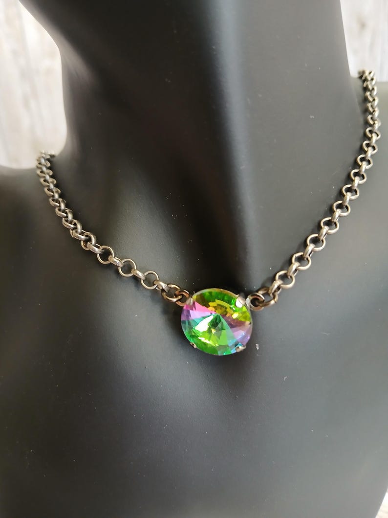 May include: A silver-toned chain necklace with a large, iridescent, oval-shaped pendant. The pendant displays a spectrum of colors, including green, yellow, and purple. The necklace is displayed on a black mannequin.