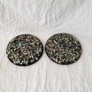 May include: Two round black coasters with a decorative design of iridescent shell pieces embedded in the surface.