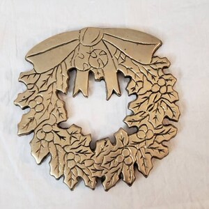 Pode incluir: Uma grinalda de metal dourado com um la&ccedil;o no topo. A grinalda &eacute; detalhada com folhas e bagas, provavelmente um item decorativo para a &eacute;poca festiva.