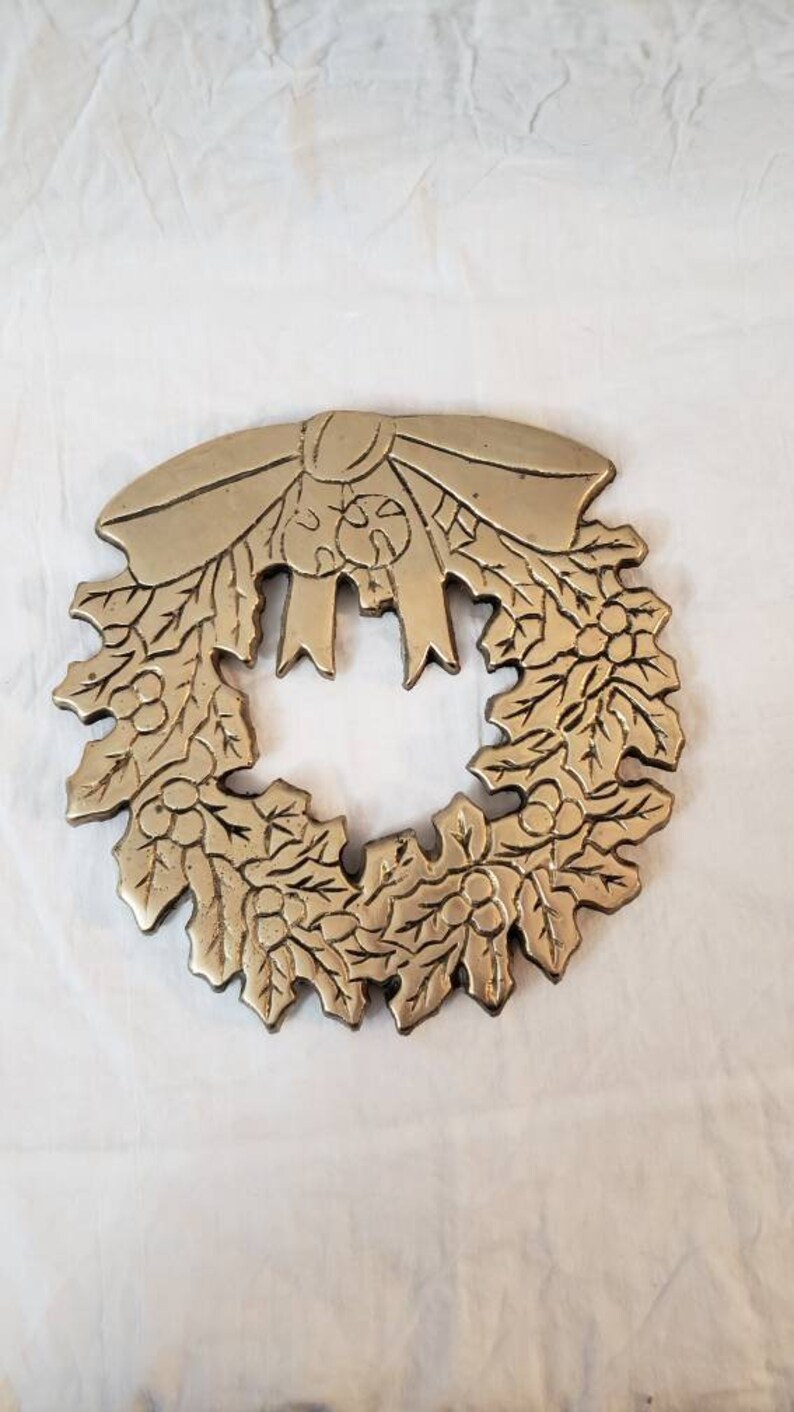 Pode incluir: Uma grinalda de metal dourado com um la&ccedil;o no topo. A grinalda &eacute; detalhada com folhas e bagas, provavelmente um item decorativo para a &eacute;poca festiva.