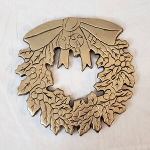 Pode incluir: Uma grinalda de metal dourado com um la&ccedil;o no topo. A grinalda &eacute; decorada com folhas e bagas, e &eacute; provavelmente um item decorativo para a &eacute;poca festiva.