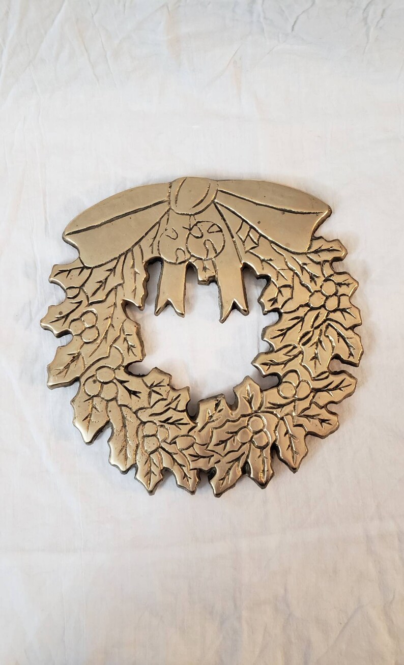 Pode incluir: Uma grinalda de metal dourado com um la&ccedil;o no topo. A grinalda &eacute; decorada com folhas e bagas, e &eacute; provavelmente um item decorativo para a &eacute;poca festiva.