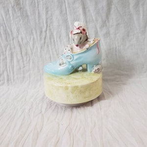 May include: A porcelain musical figurine of a mouse wearing a pink and white bonnet sitting in a blue shoe. Two smaller mice are on the base of the shoe.