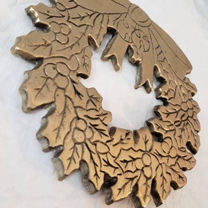 Pode incluir: Uma coroa detalhada, em tom bronze, com um design de folhas e bagas. A coroa &eacute; circular com um la&ccedil;o no topo. O metal tem uma apar&ecirc;ncia texturizada e envelhecida, sugerindo que &eacute; vintage ou antigo. A coroa &eacute; provavelmente usada para fins decorativos.