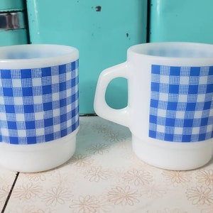 May include: Two white ceramic mugs with a blue and white gingham pattern.