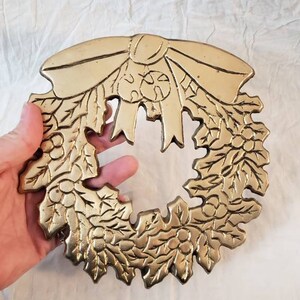 Pode incluir: Uma grinalda de metal dourado com um la&ccedil;o no topo. A grinalda &eacute; decorada com folhas e bagas. A grinalda tem aproximadamente 20 cm de di&acirc;metro.