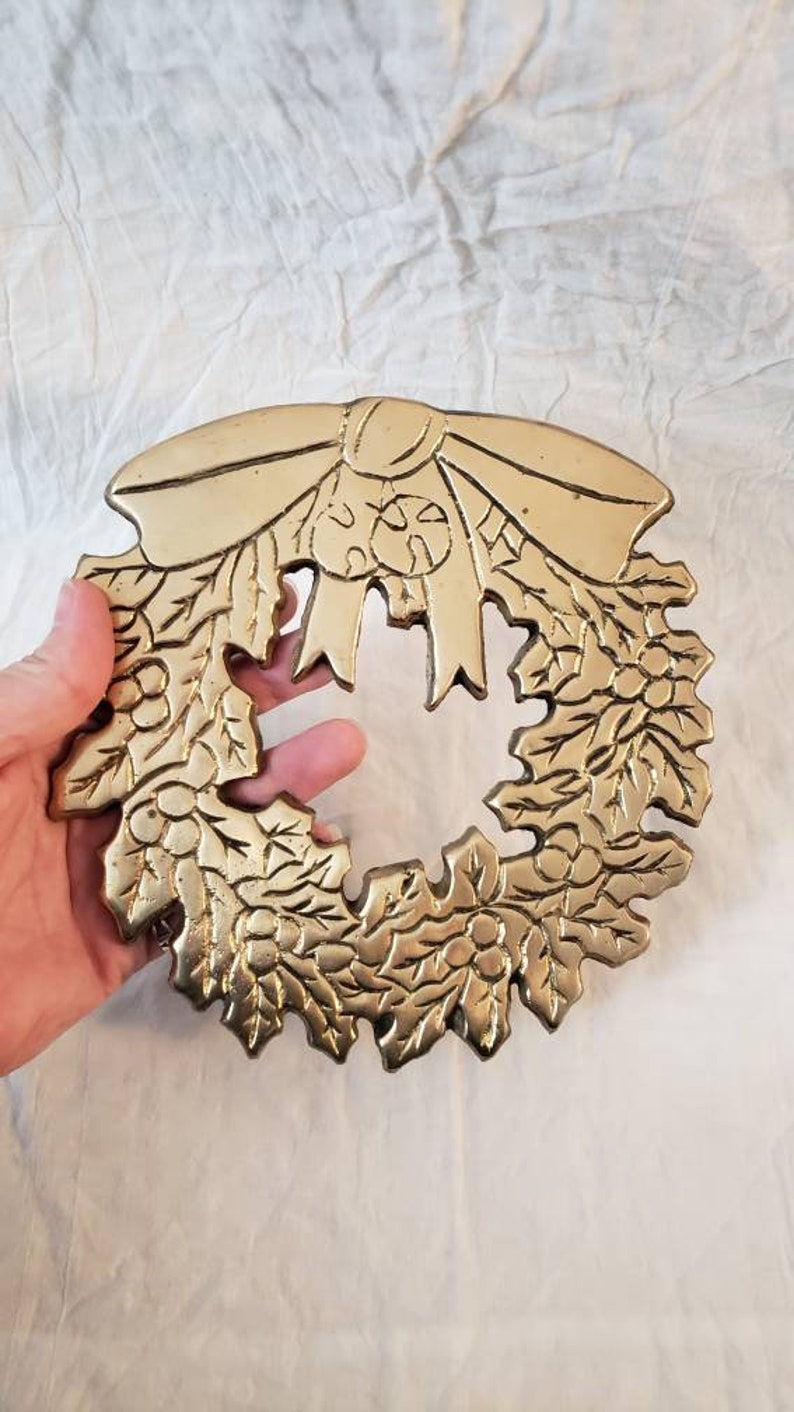 Pode incluir: Uma grinalda de metal dourado com um la&ccedil;o no topo. A grinalda &eacute; decorada com folhas e bagas. A grinalda tem aproximadamente 20 cm de di&acirc;metro.