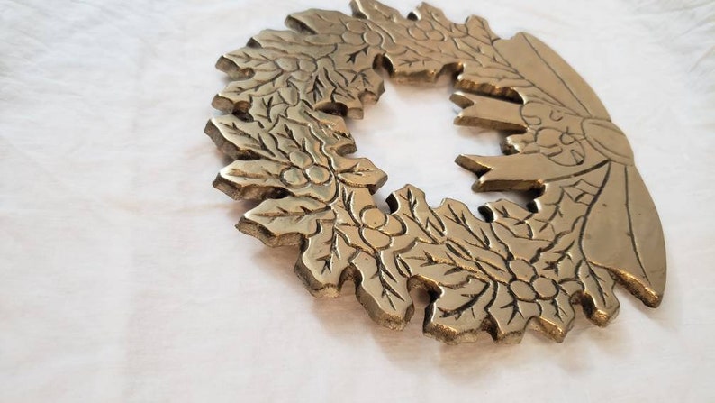 Pode incluir: Uma detalhada coroa de metal dourado com um design de folhas e bagas. A coroa &eacute; circular, com uma sec&ccedil;&atilde;o em falta, e assenta numa superf&iacute;cie branca. O design &eacute; intrincado e parece ser de metal fundido.