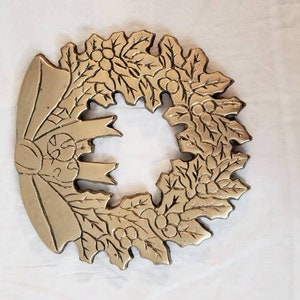Pode incluir: Uma grinalda de metal dourado com um la&ccedil;o no lado esquerdo. A grinalda &eacute; decorada com folhas e bagas, e &eacute; provavelmente uma decora&ccedil;&atilde;o de Natal. A grinalda est&aacute; sobre uma superf&iacute;cie branca.