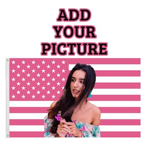 May include: A pink and white American flag with the text "ADD YOUR PICTURE" in black and pink. A person is in front of the flag, holding a flower. The flag has a grommet on the left side.