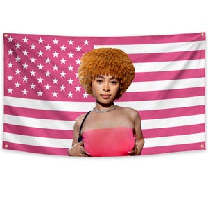 May include: A pink and white American flag with a woman in front of it. The woman is wearing a pink tube top and a silver necklace. She has curly orange hair.