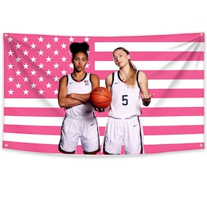 Pode incluir: Uma tapeçaria retangular com um design de bandeira americana em rosa e branco. Dois jogadores de basquete com camisas e shorts brancos posam em frente à bandeira. Um segura uma bola de basquete laranja e o outro tem os braços cruzados.