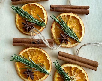 May include: Four handmade ornaments featuring dried orange slices, each topped with two brown cinnamon sticks, a sprig of green rosemary, and a dark brown star anise. Each ornament includes a natural jute twine loop for hanging purposes.