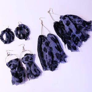 May include: An assortment of handmade earrings in various styles. The earrings feature a combination of blue and black fabric, some with a leopard print design. The earrings are displayed on a white surface.