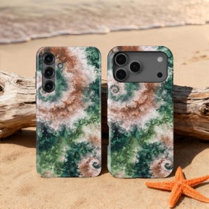Puede incluir: Dos fundas para teléfono con un diseño de teñido anudado en espiral en tonos verdes, marrones y blancos. Se muestran en una playa de arena con una estrella de mar y madera flotante en el fondo.